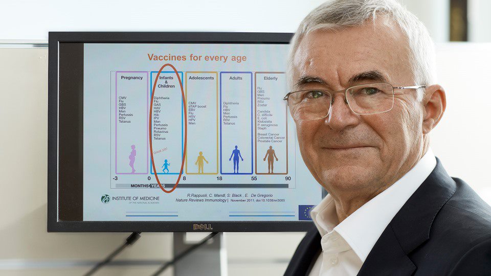 Inventor smiling in front of a screen showing information about vaccines