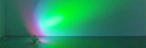 Lamp standing on floor shining onto wall, breaking the light into different colours such as purple, bright blue, but mainly vivid green